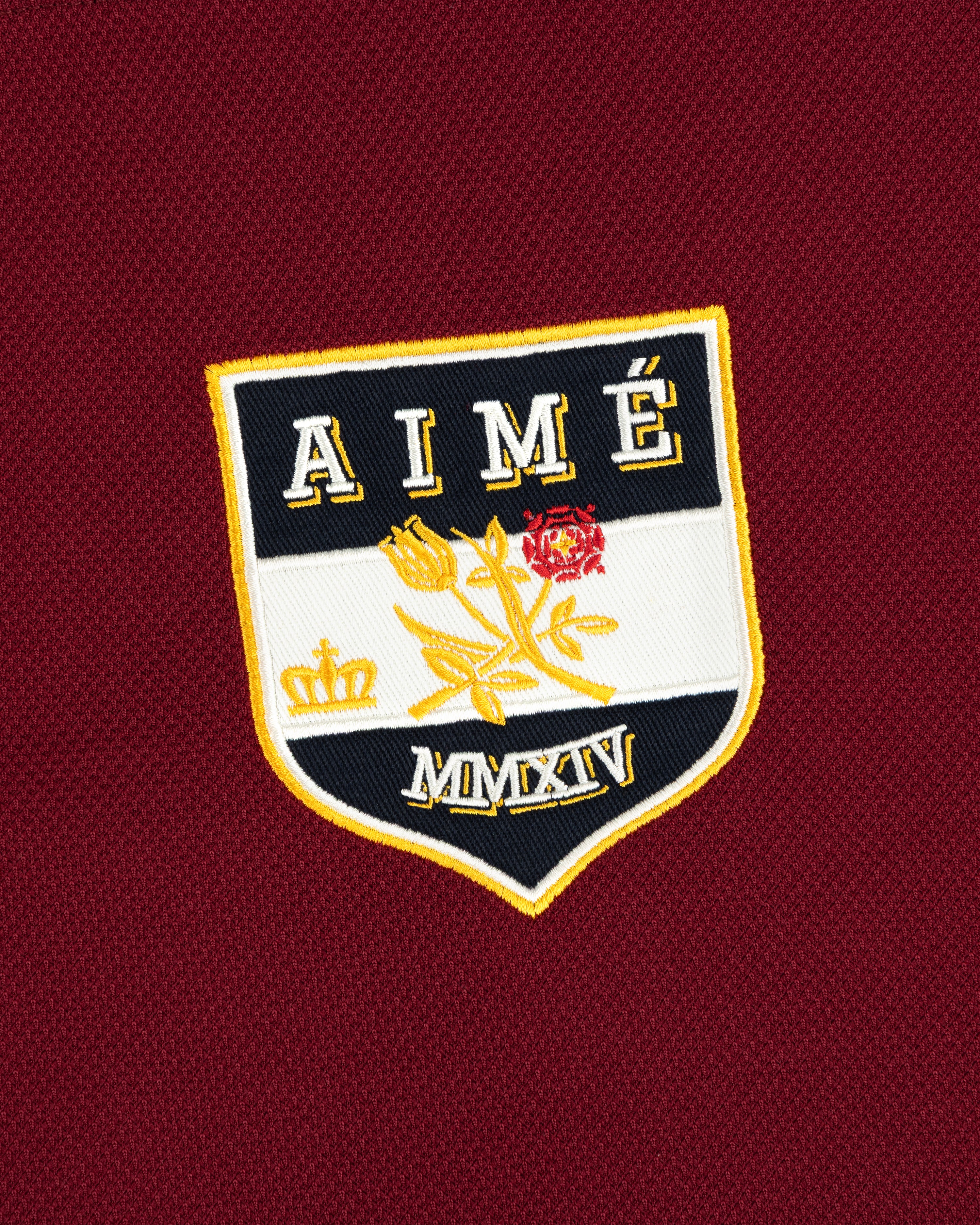 Team Aimé Hockey Jersey featuring a maroon textured fabric and a shield-shaped crest with flowers, a crown, AIMÉ, and MMXIV.