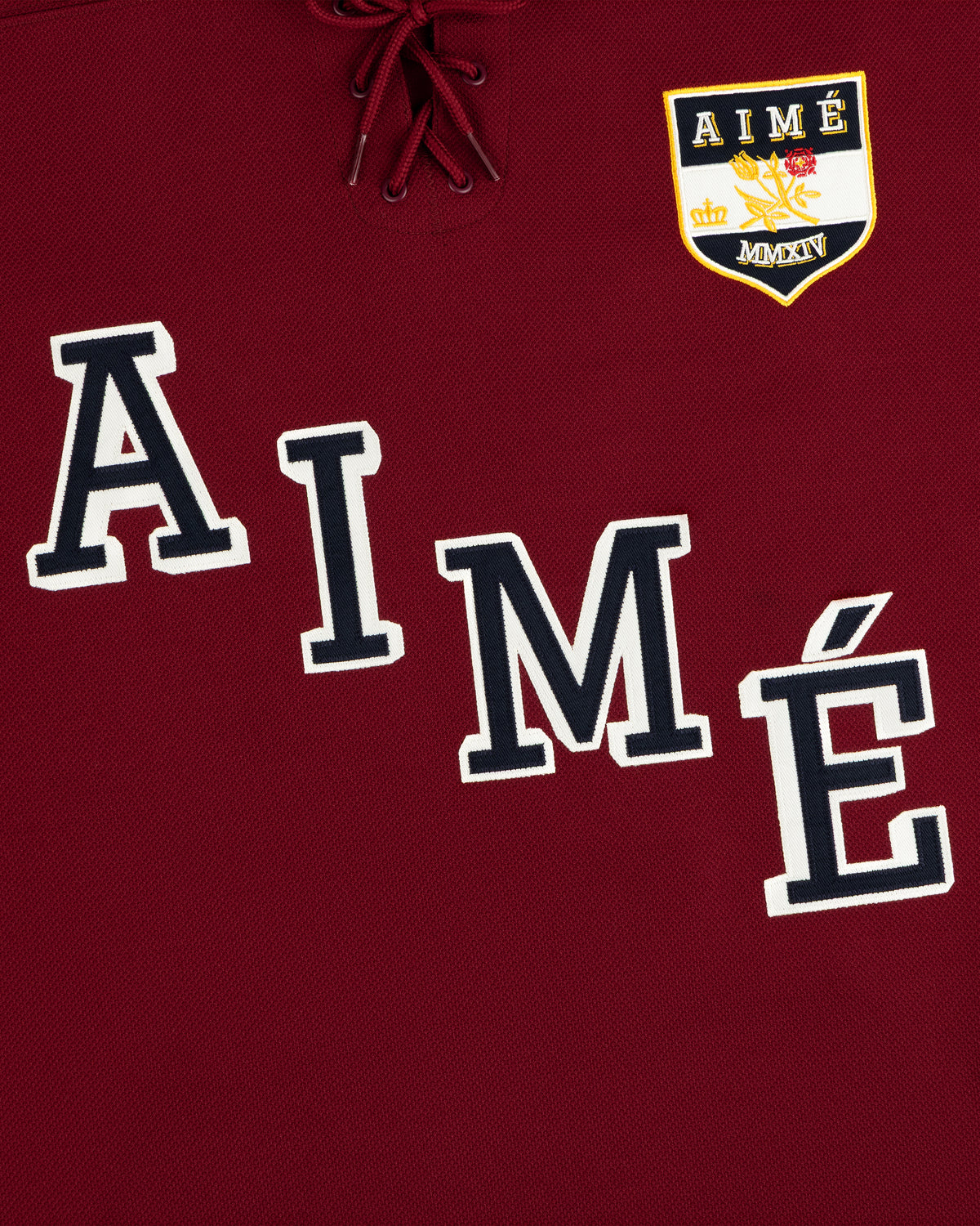 Team Aimé Hockey Jersey in maroon with a lace-up neck, the word AIME, and a crest with a crown and floral graphic.