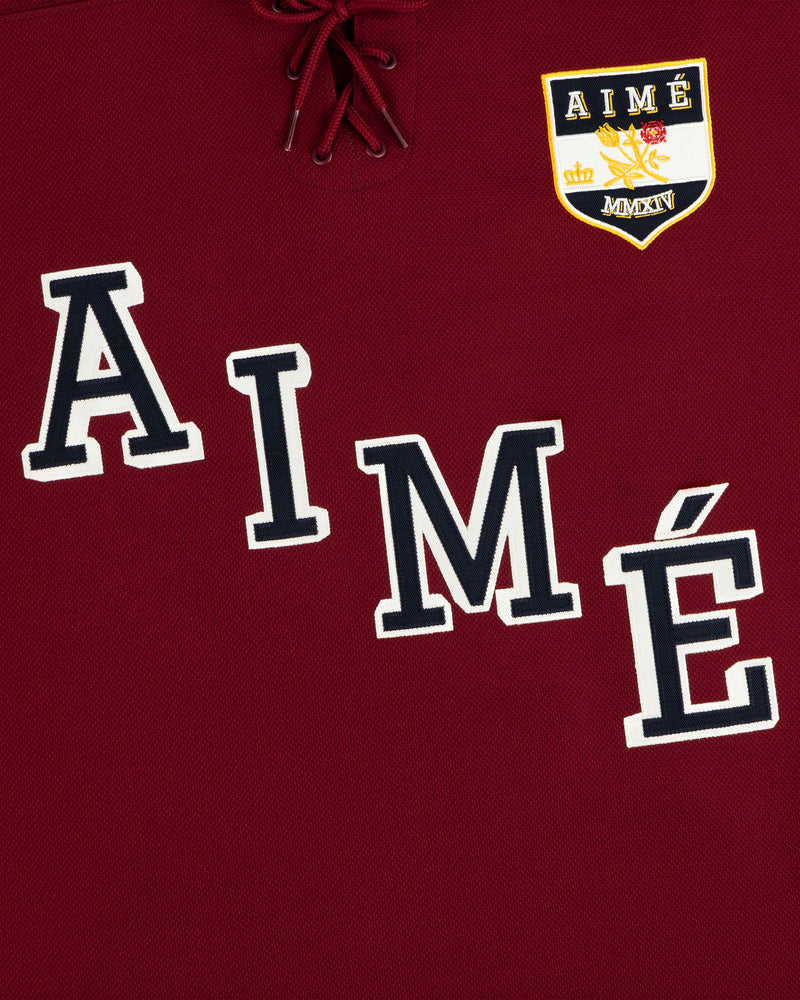 Team Aimé Hockey Jersey in maroon with a lace-up neck, the word AIME, and a crest with a crown and floral graphic.