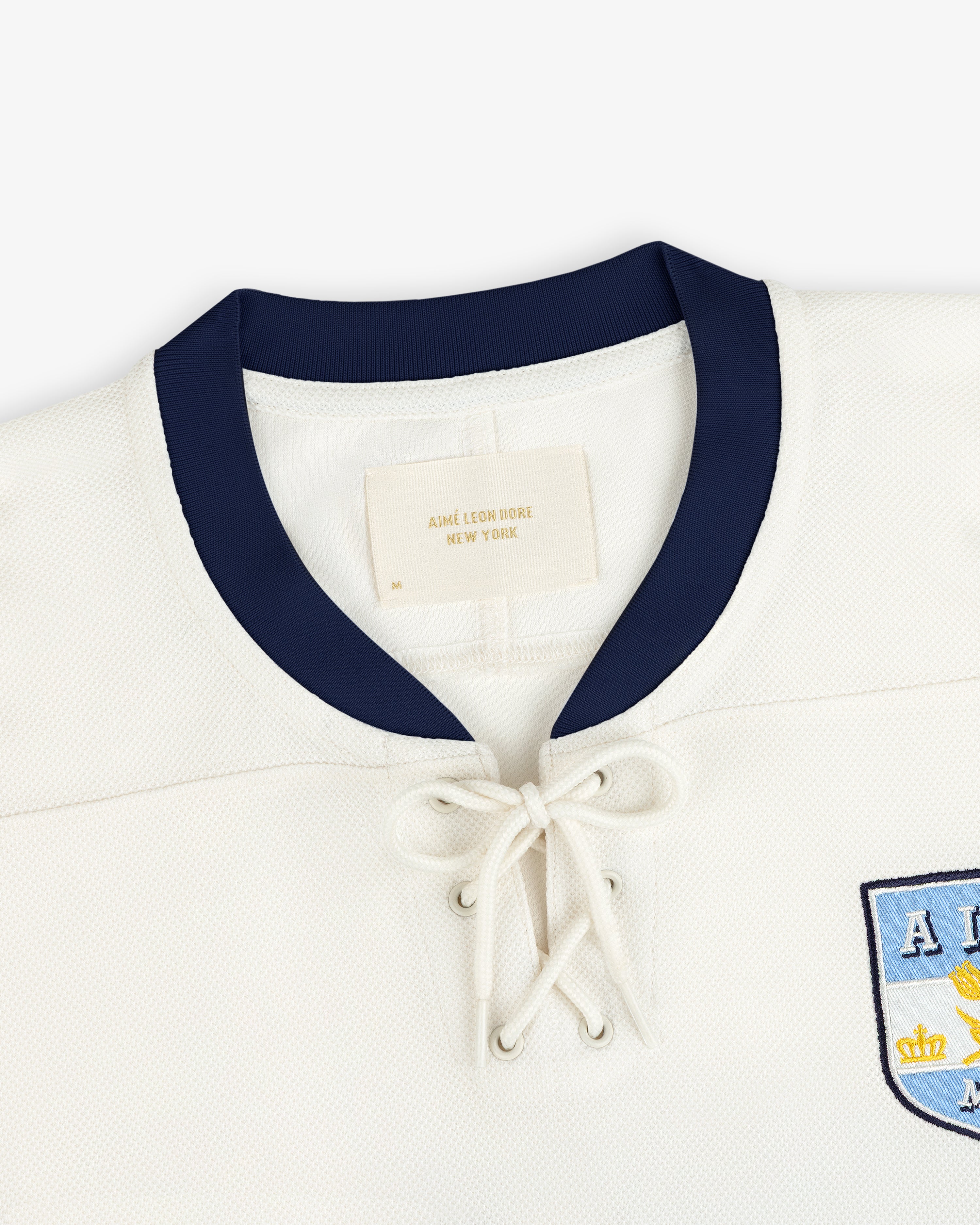 Team Aimé Hockey Jersey in off-white with a dark blue collar, lace-up neckline, and a chest emblem.