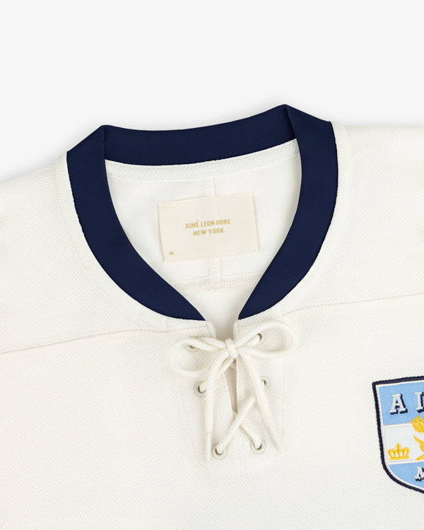 Team Aimé Hockey Jersey in off-white with a dark blue collar, lace-up neckline, and a chest emblem.