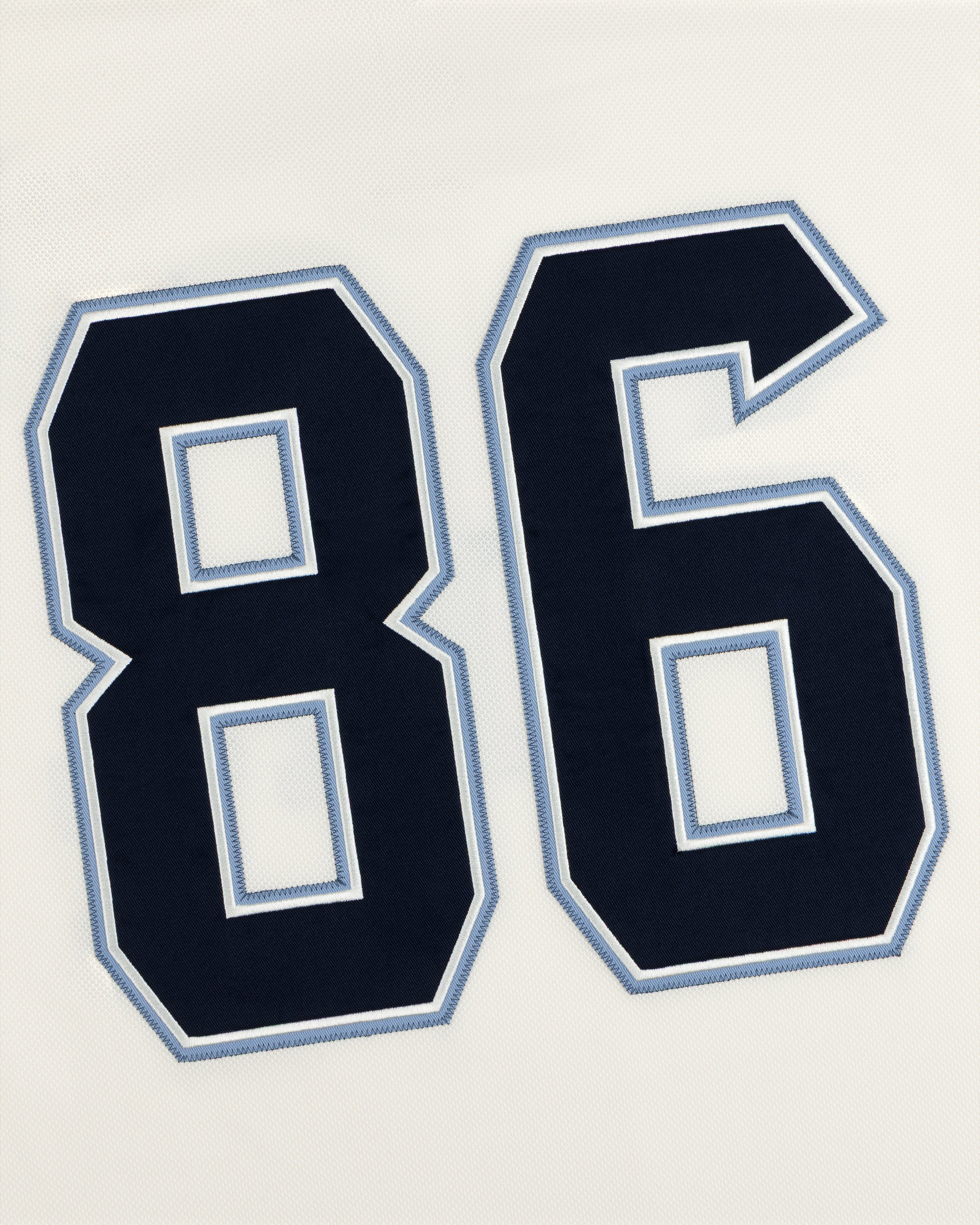 The number 86 in dark navy blue with light blue and white outlines on a white Team Aimé Hockey Jersey.