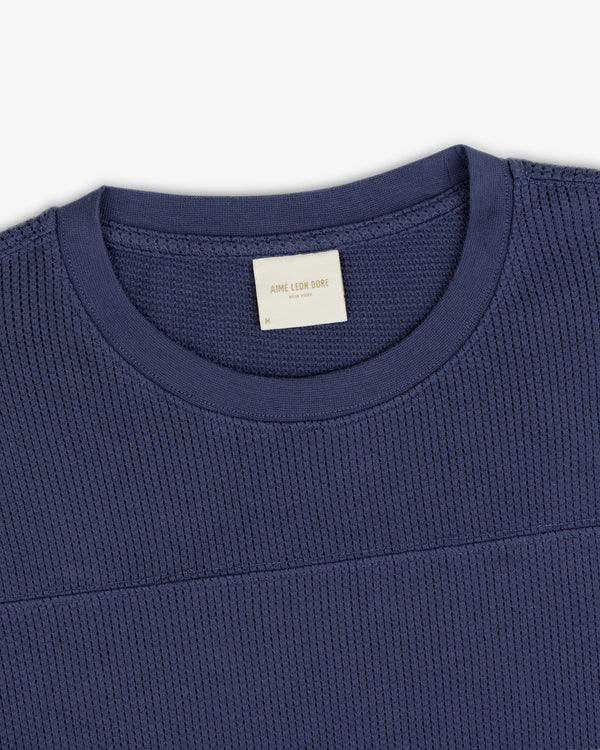 Close-up of a navy Long-Sleeve Mesh Football Tee with a visible Aimé Leon Dore label on the collar.