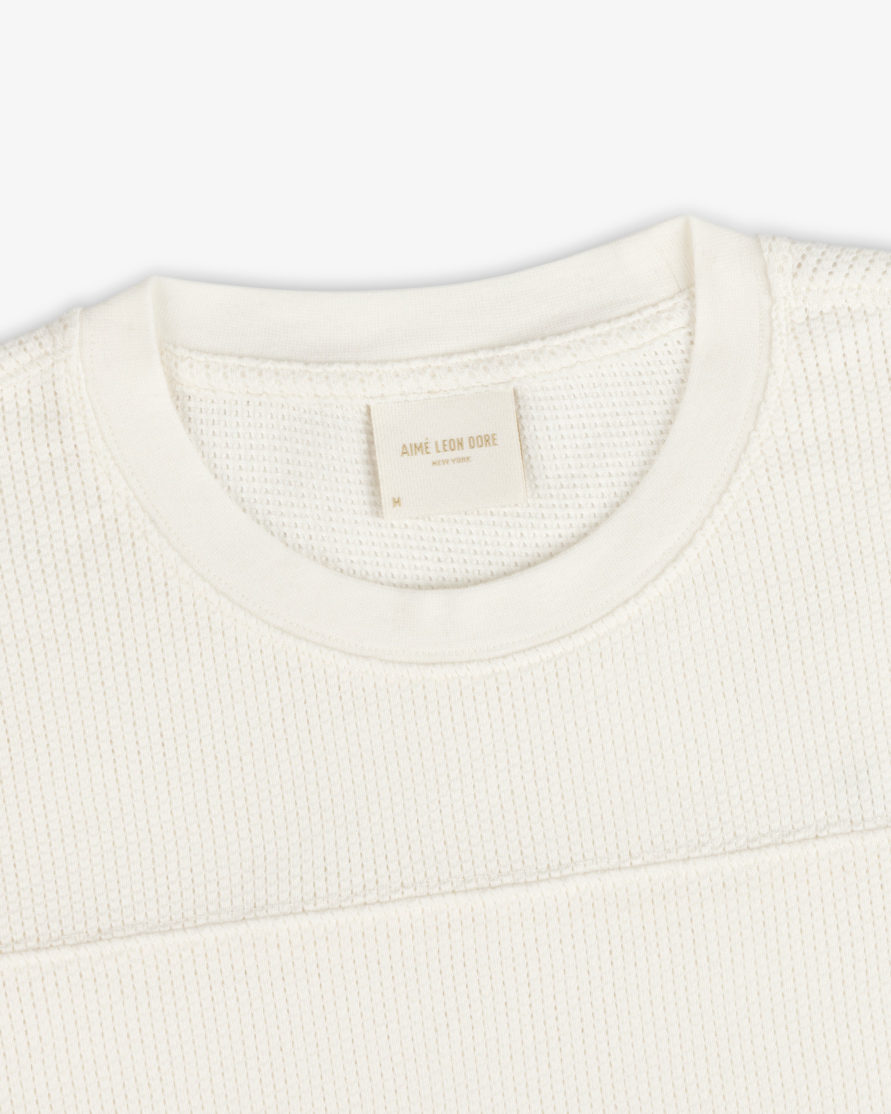 Close-up of a Long-Sleeve Mesh Football Tee in cream, featuring a visible brand tag inside the crewneck collar.