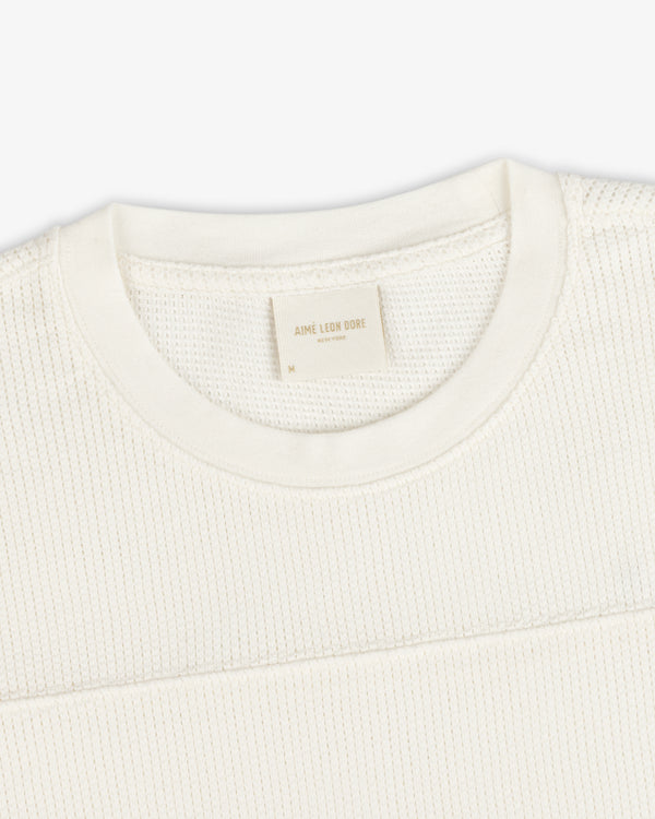 Close-up of a Long-Sleeve Mesh Football Tee in cream, featuring a visible brand tag inside the crewneck collar.
