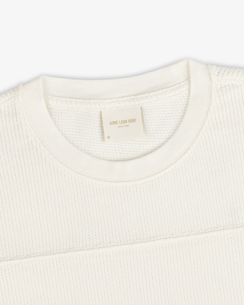Close-up of a Long-Sleeve Mesh Football Tee in cream, featuring a visible brand tag inside the crewneck collar.