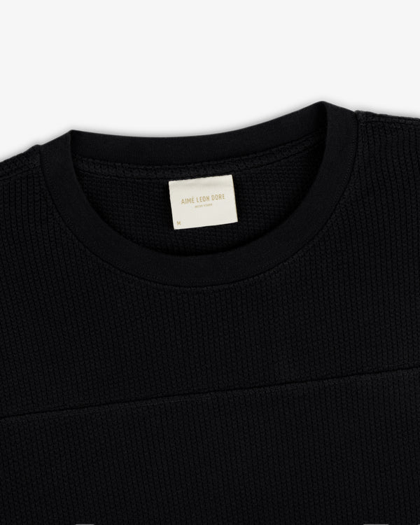 Close-up of a black Long-Sleeve Mesh Football Tee with a visible white Aime Leon Dore label inside the collar.