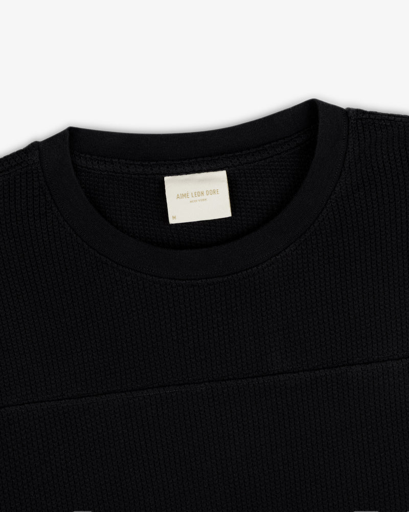 Close-up of a black Long-Sleeve Mesh Football Tee with a visible white Aime Leon Dore label inside the collar.