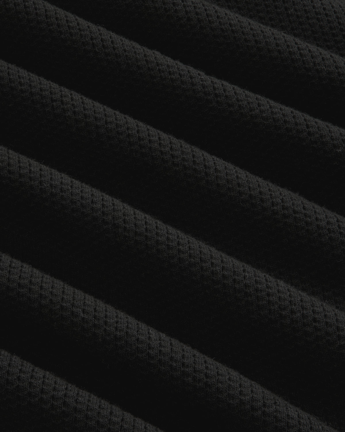 Close-up of black ribbed mesh fabric with diagonal folds on the Long-Sleeve Mesh Football Tee.