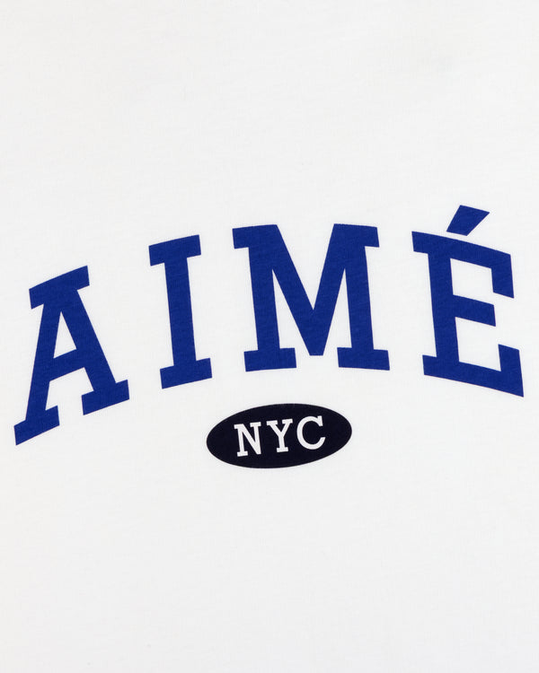 White tee with bold blue AIMÉ above a small black oval showing NYC in white—Aimé Souvenir Tee.