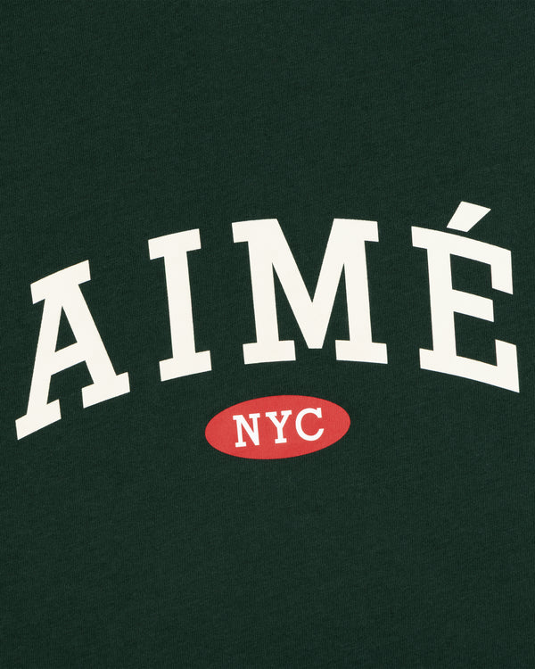 Aimé Souvenir Tee: white AIMÉ text and red NYC oval on dark green.