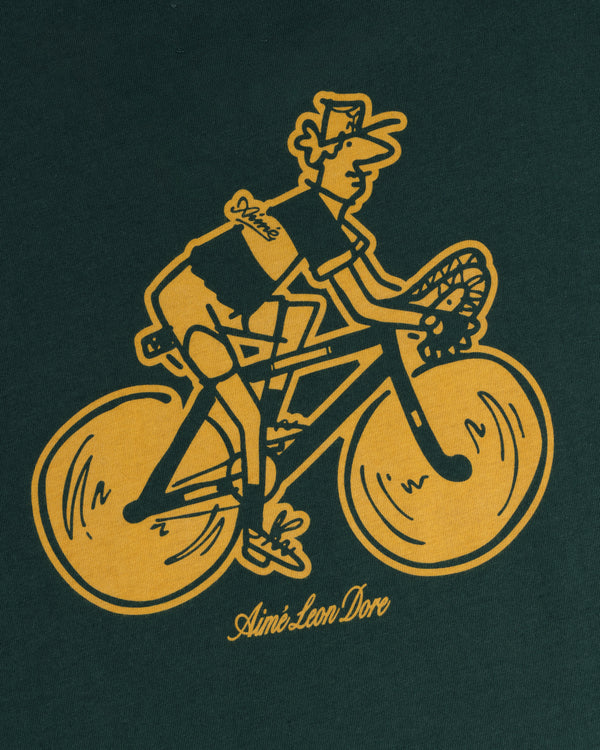 Yellow mailman on bike graphic with “Aimé Leon Dore” below, featured on the Aimé Tour Graphic Tee’s dark green background.