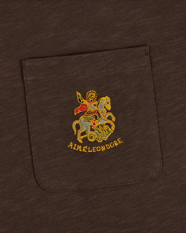 Brown Saint George Slub Pocket Tee featuring colorful horseback figure embroidery and AIME LEON DORE text below.