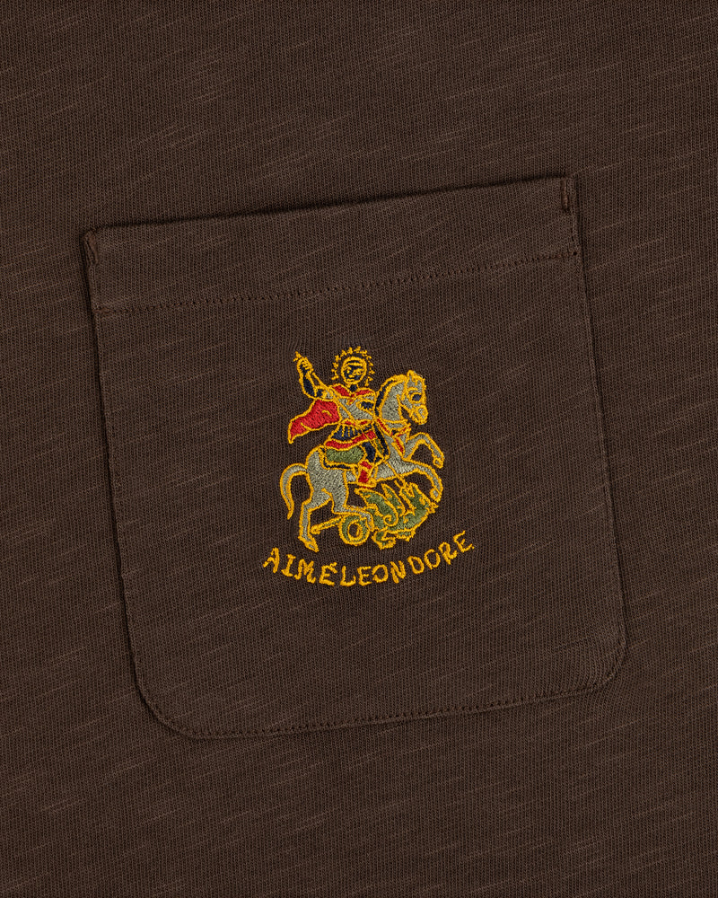 Brown Saint George Slub Pocket Tee featuring colorful horseback figure embroidery and AIME LEON DORE text below.