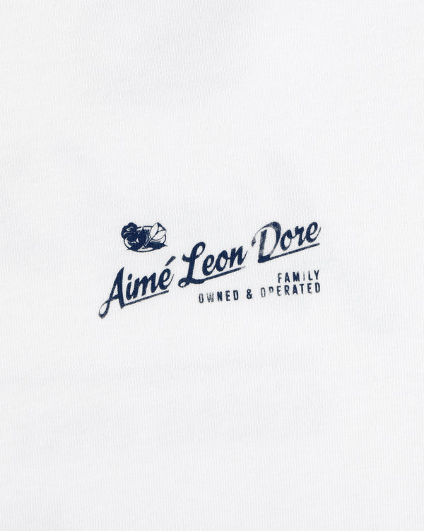 Neighborhood Tee: Small navy Aimé Leon Dore logo, boat & “Family Owned & Operated” on white fabric.