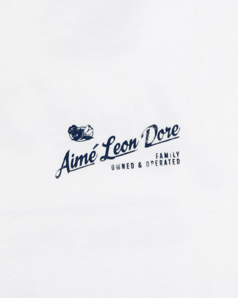 Neighborhood Tee: Small navy Aimé Leon Dore logo, boat & “Family Owned & Operated” on white fabric.