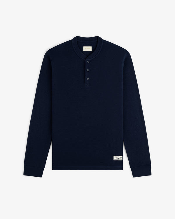 Navy blue Long-Sleeve Waffle Henley with a three-button placket and a small rectangular logo patch on the hem.