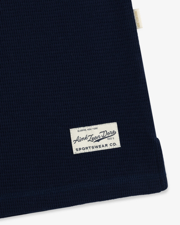 Close-up of a navy blue Long-Sleeve Waffle Henley with a rectangular brand patch on the lower front.
