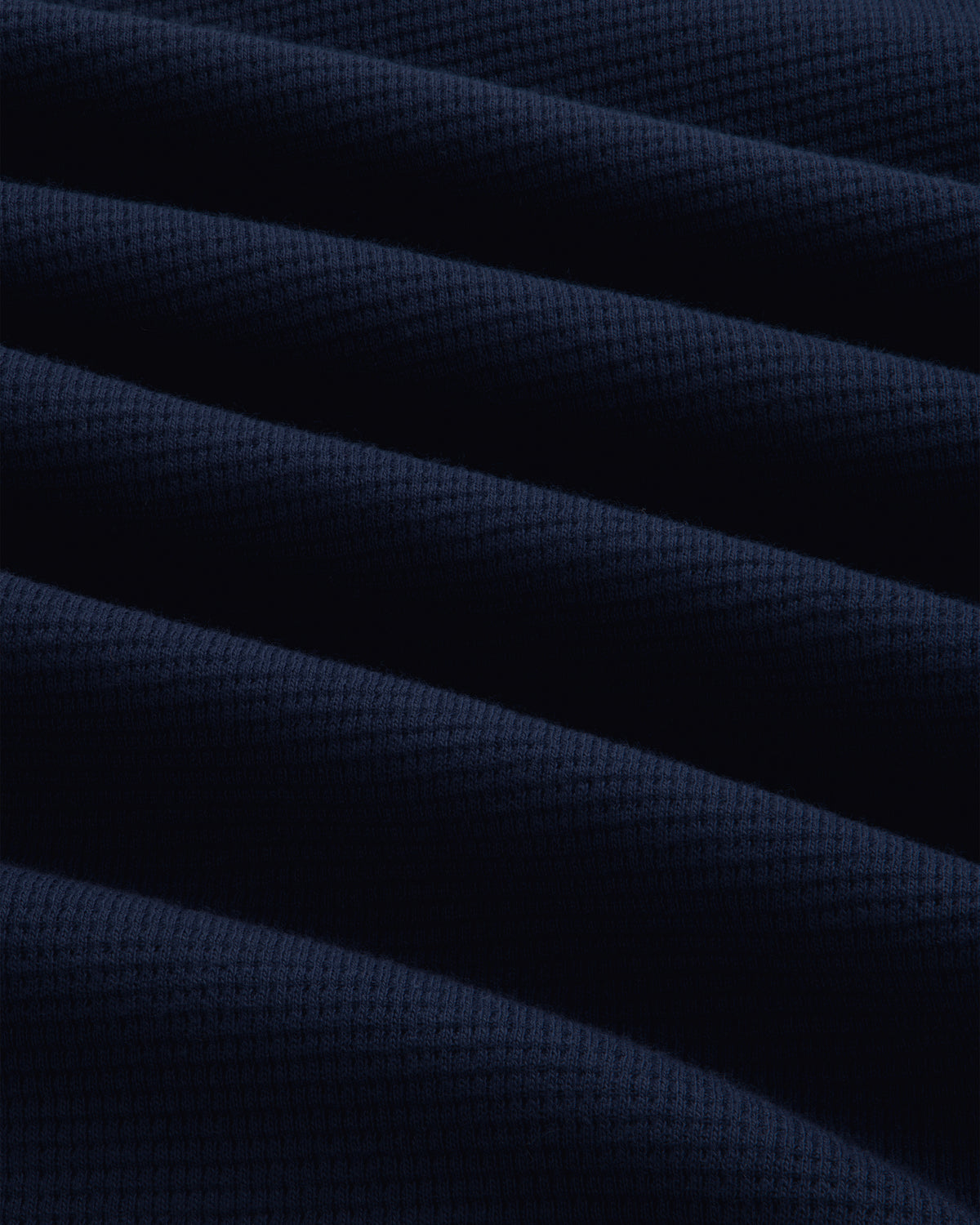 Close-up of a dark blue Long-Sleeve Waffle Henley with a waffle-knit texture and soft folds.