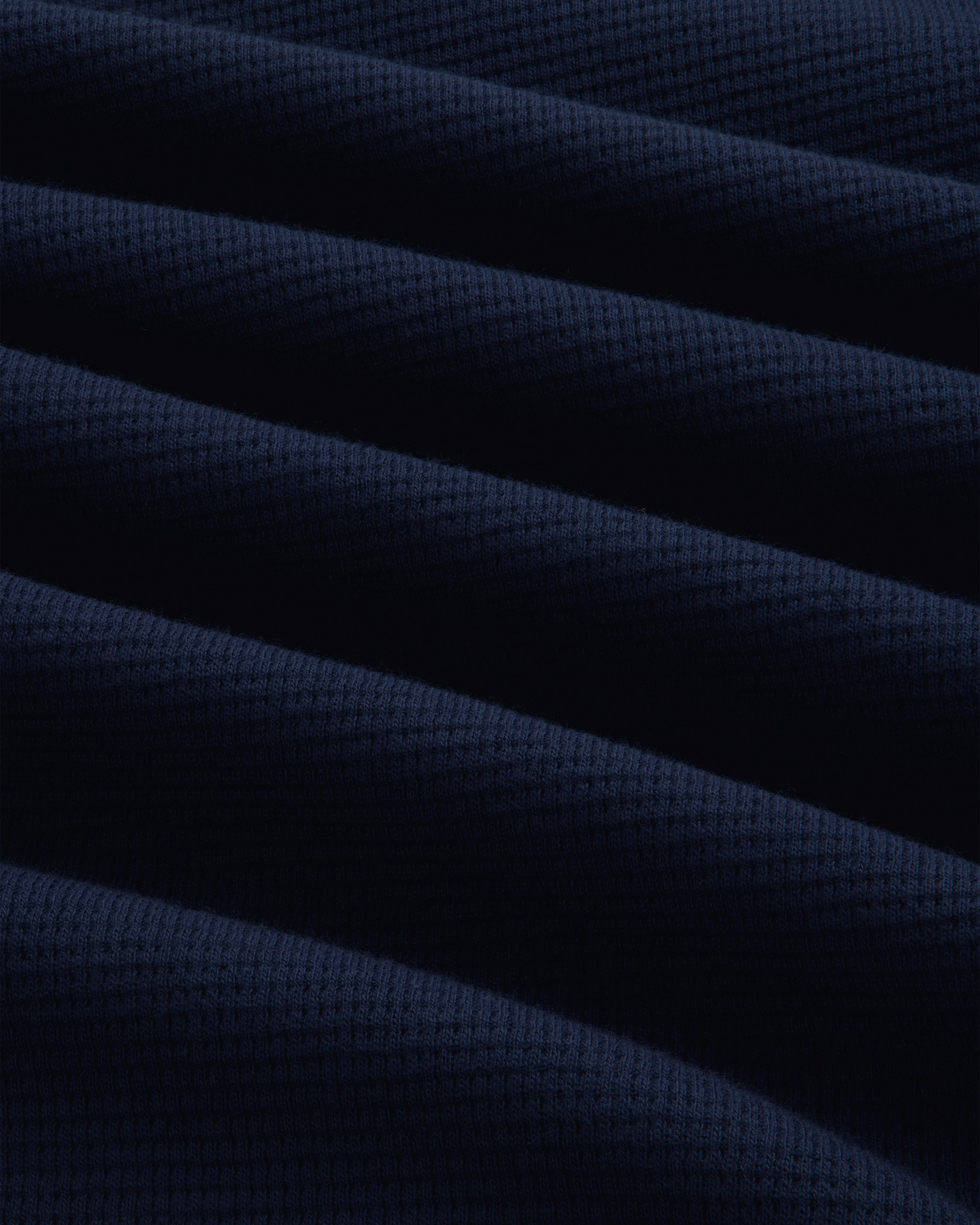 Close-up of a dark blue Long-Sleeve Waffle Henley with a waffle-knit texture and soft folds.