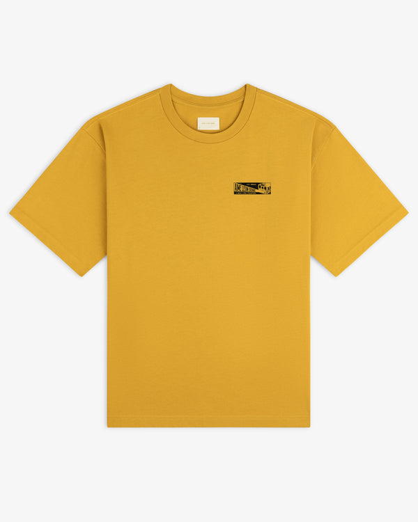 Mustard yellow Aimé Transit Tee with a short-sleeve crewneck and a small rectangular graphic on the left chest.