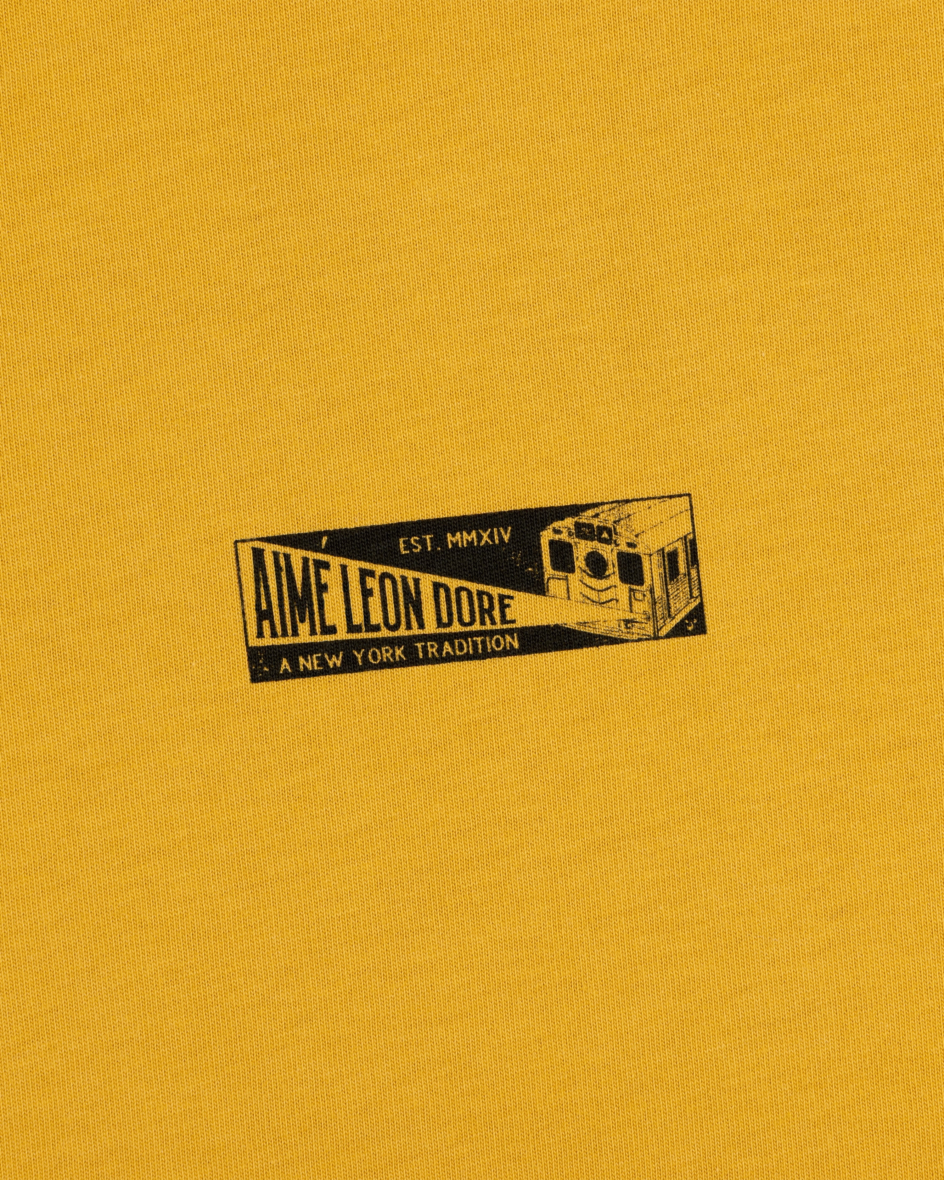 Mustard yellow Aimé Transit Tee featuring a graphic of a New York subway car with the text Aime Leon Dore, Est. MMXIV.