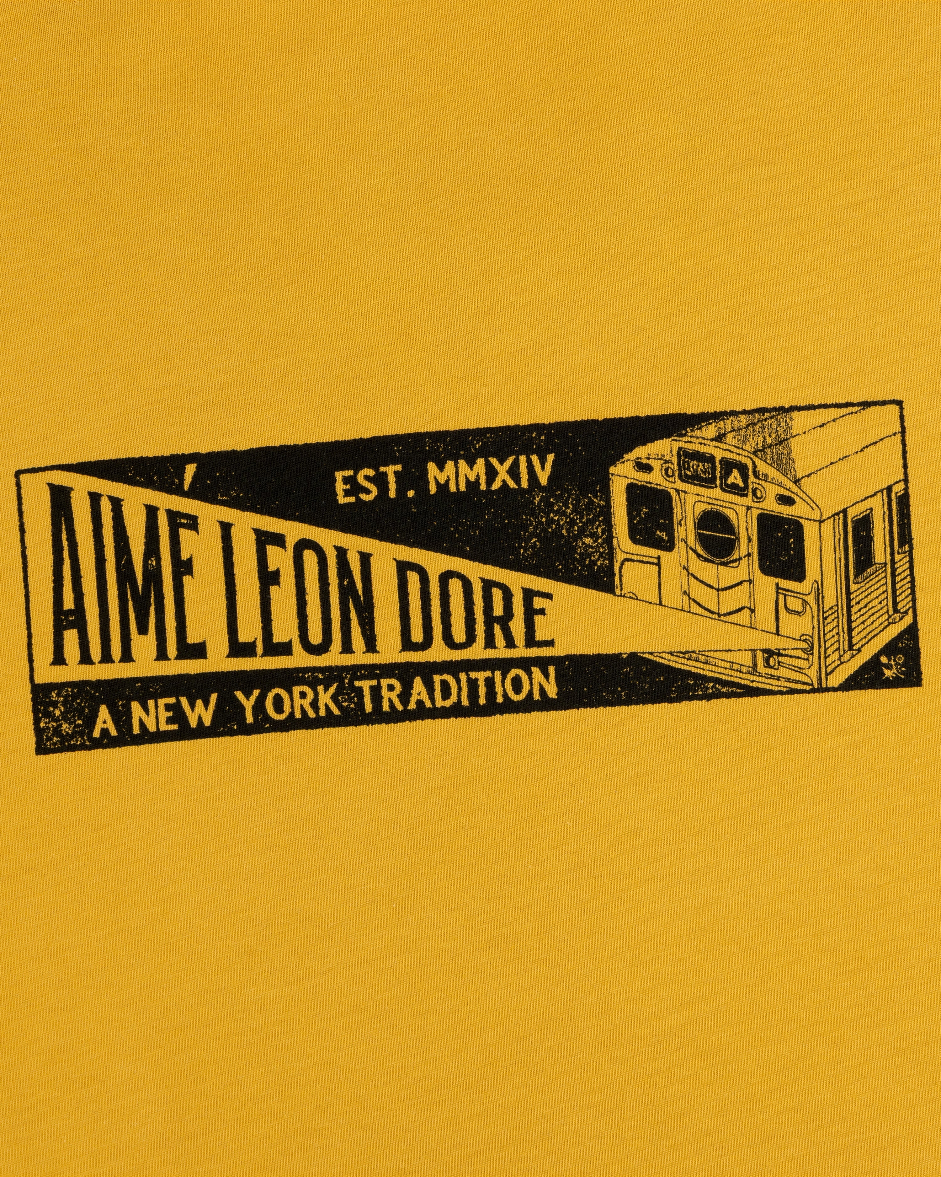 Mustard yellow Aimé Transit Tee with a subway car graphic and text: Aime Leon Dore, Est. MMXIV, A New York Tradition.
