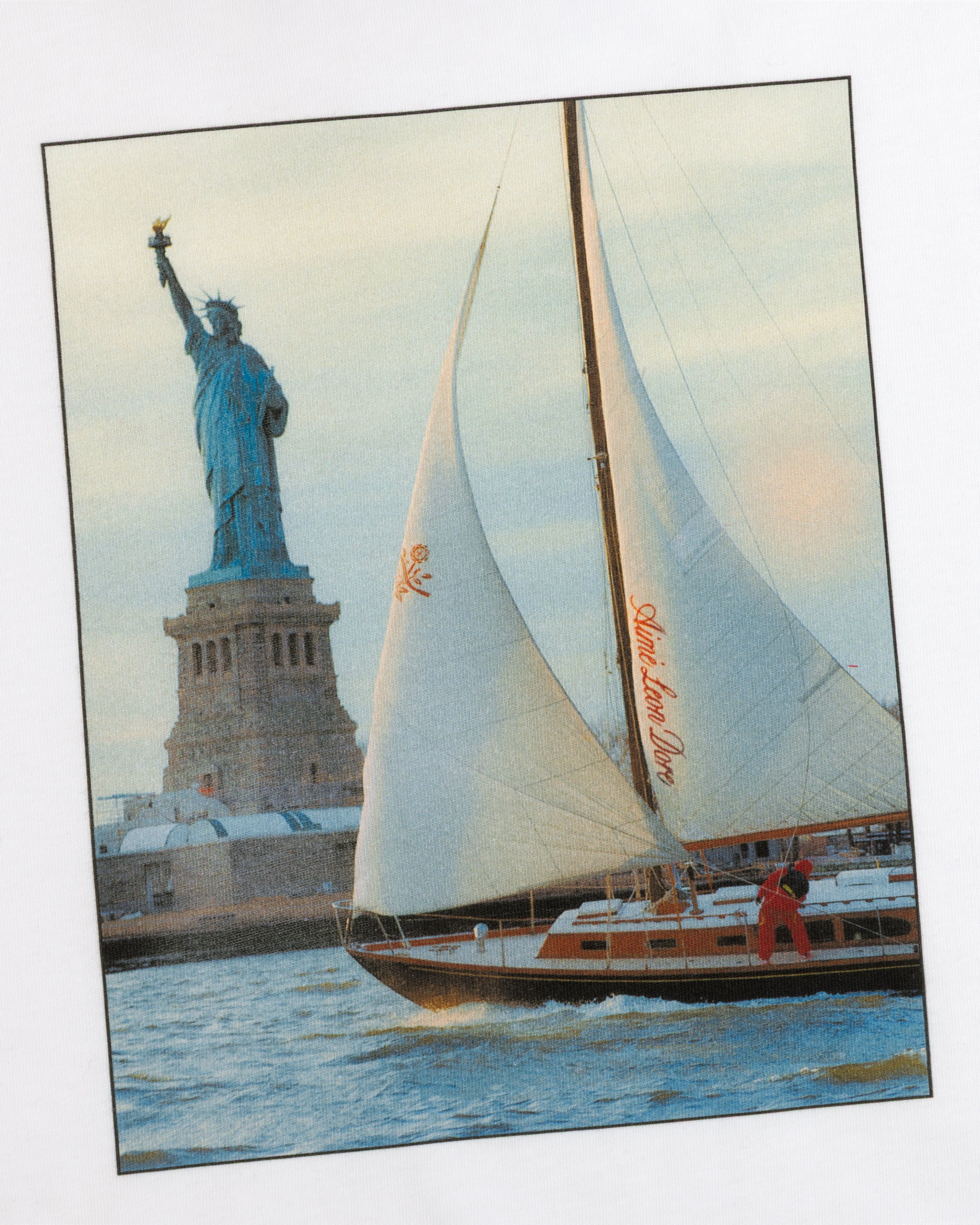 A person wearing a Long-Sleeve Sailing Tee on a sailboat passing the Statue of Liberty.