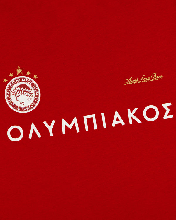 ALD / Olympiacos F.C. Souvenir Tee in red featuring a circular team crest with three gold stars and OLYMPIAKOS text.