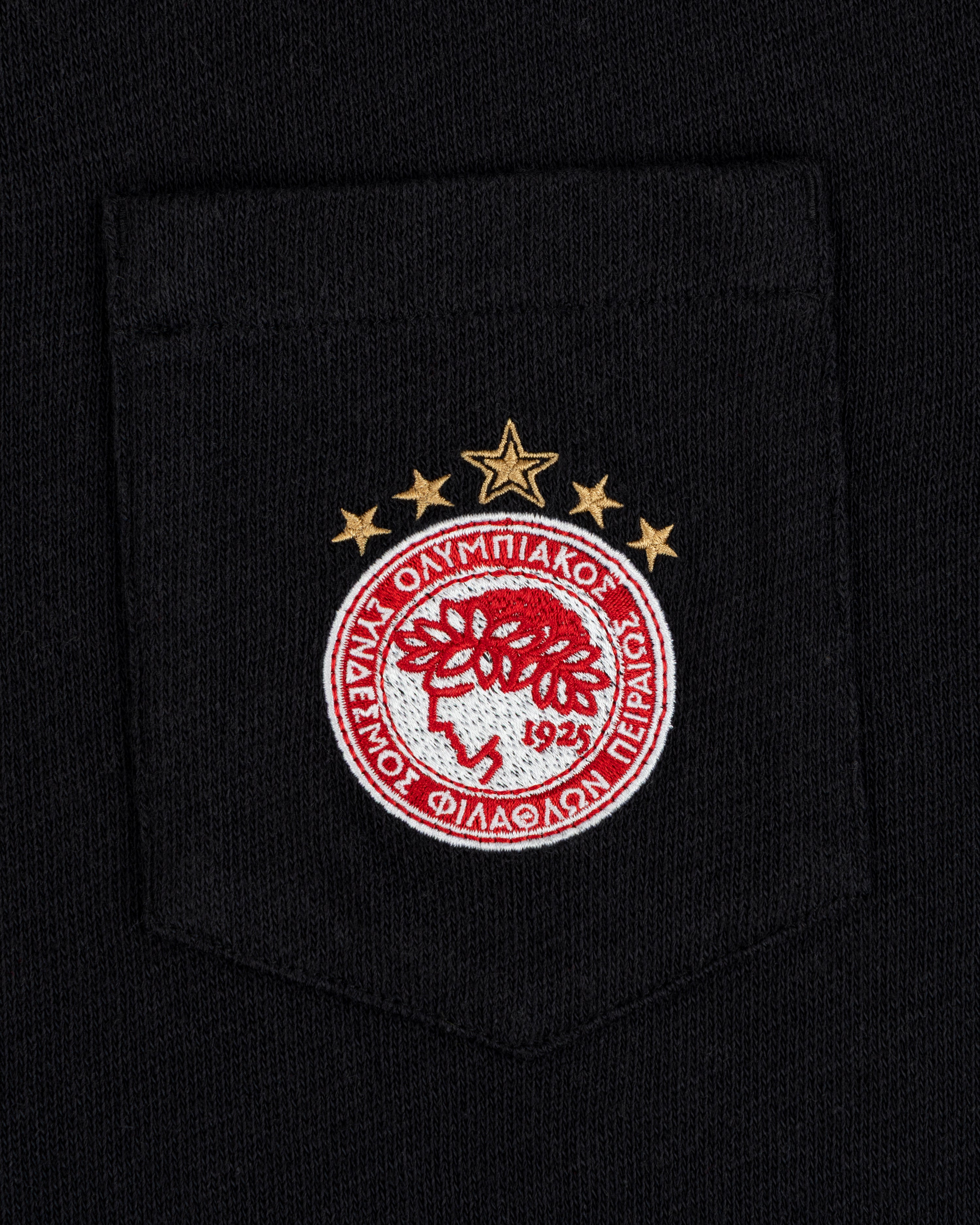 An ALD / Olympiacos F.C. Heritage Ringer Polo pocket featuring an embroidered crest, laurel wreath, Greek text, and stars.