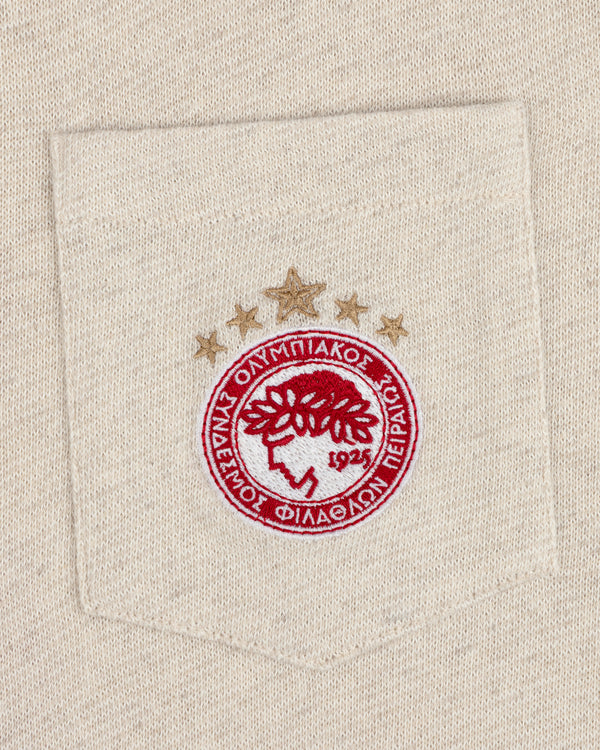 Embroidered red and gold crest with stars on the beige pocket of an ALD/Olympiacos F.C. Heritage Ringer Polo.