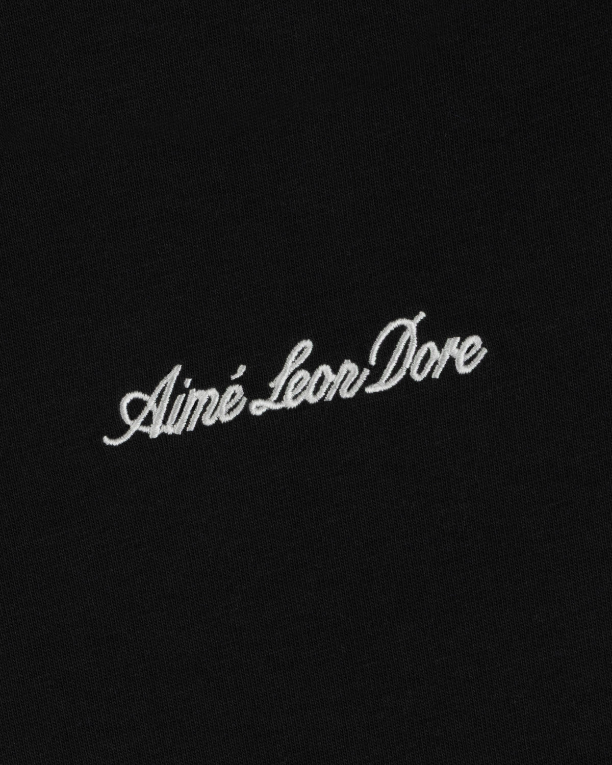 White embroidered Shrunken Script Tee lettering on a black fabric background.