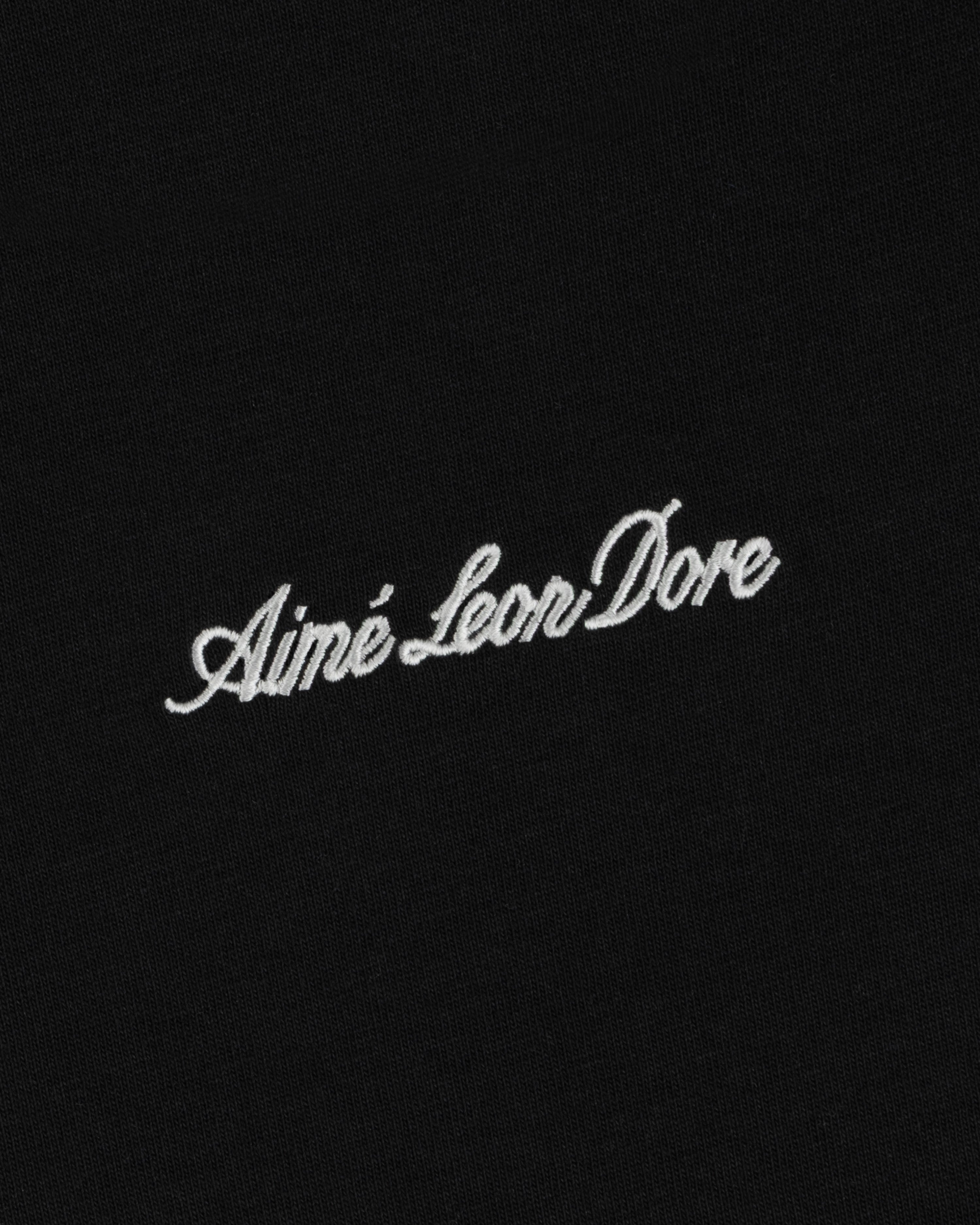 White embroidered Shrunken Script Tee lettering on a black fabric background.