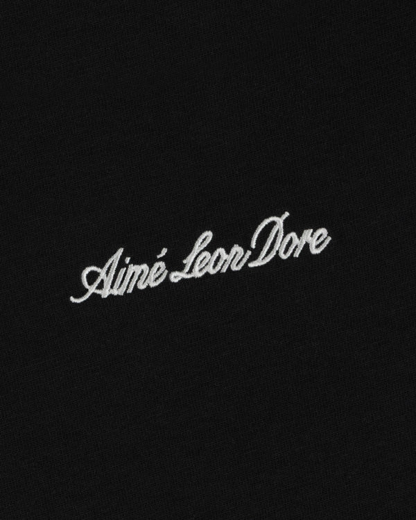 White embroidered Shrunken Script Tee lettering on a black fabric background.