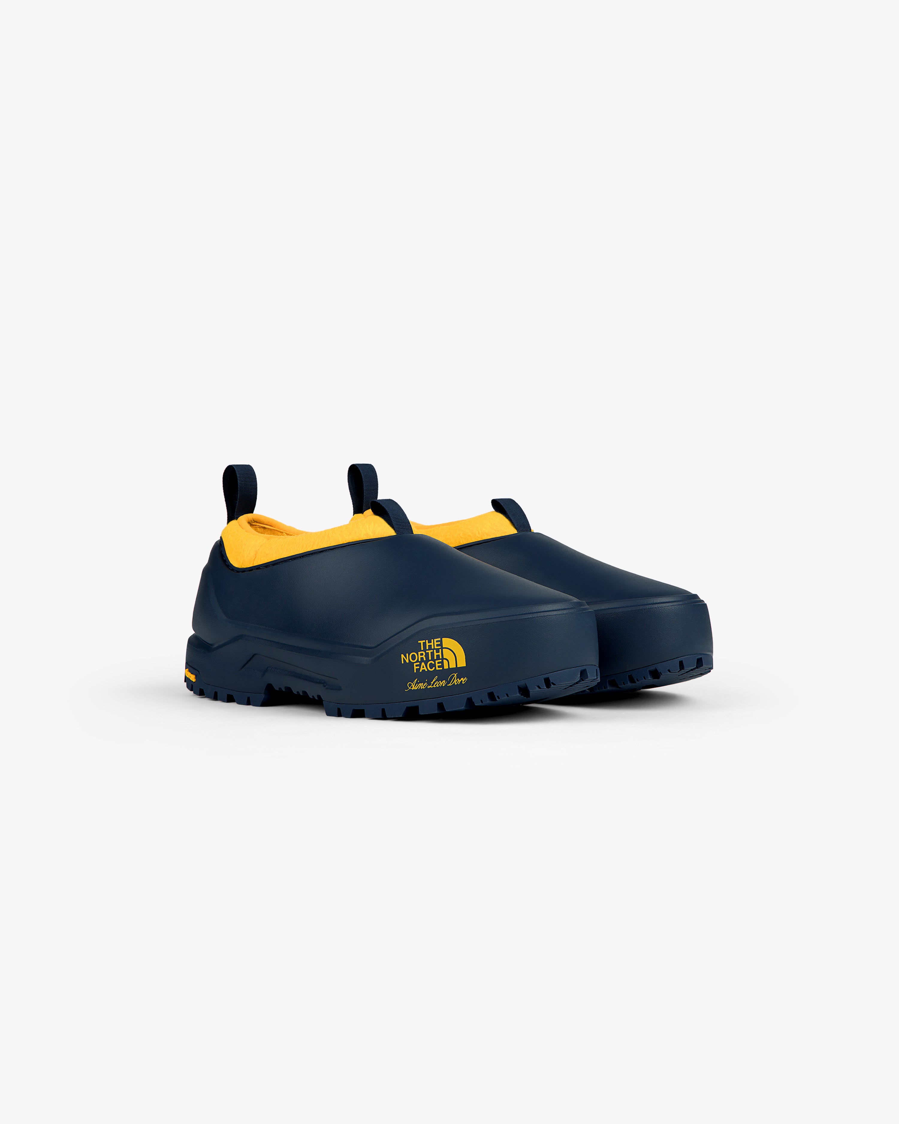 ALD / The North Face Base Camp Mule: dark blue slip-ons with yellow lining, rugged soles, logo on side.