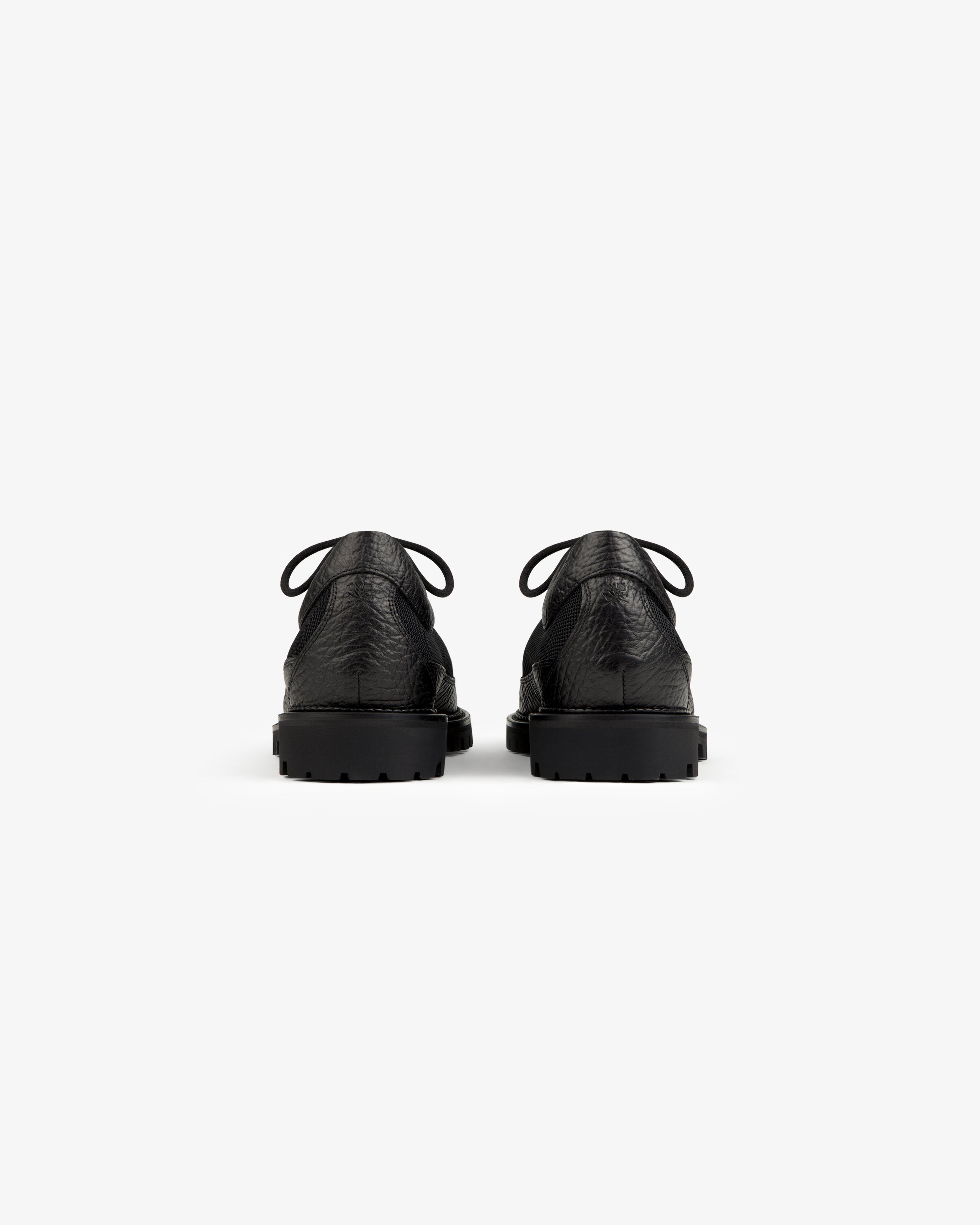 Back view of two black leather Field Boot lace-up boots with thick rubber lug soles.