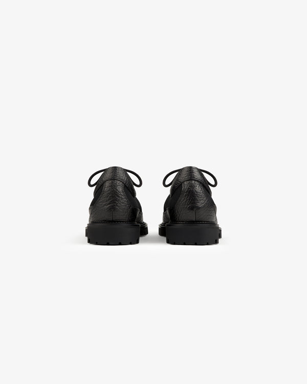 Back view of two black leather Field Boot lace-up boots with thick rubber lug soles.