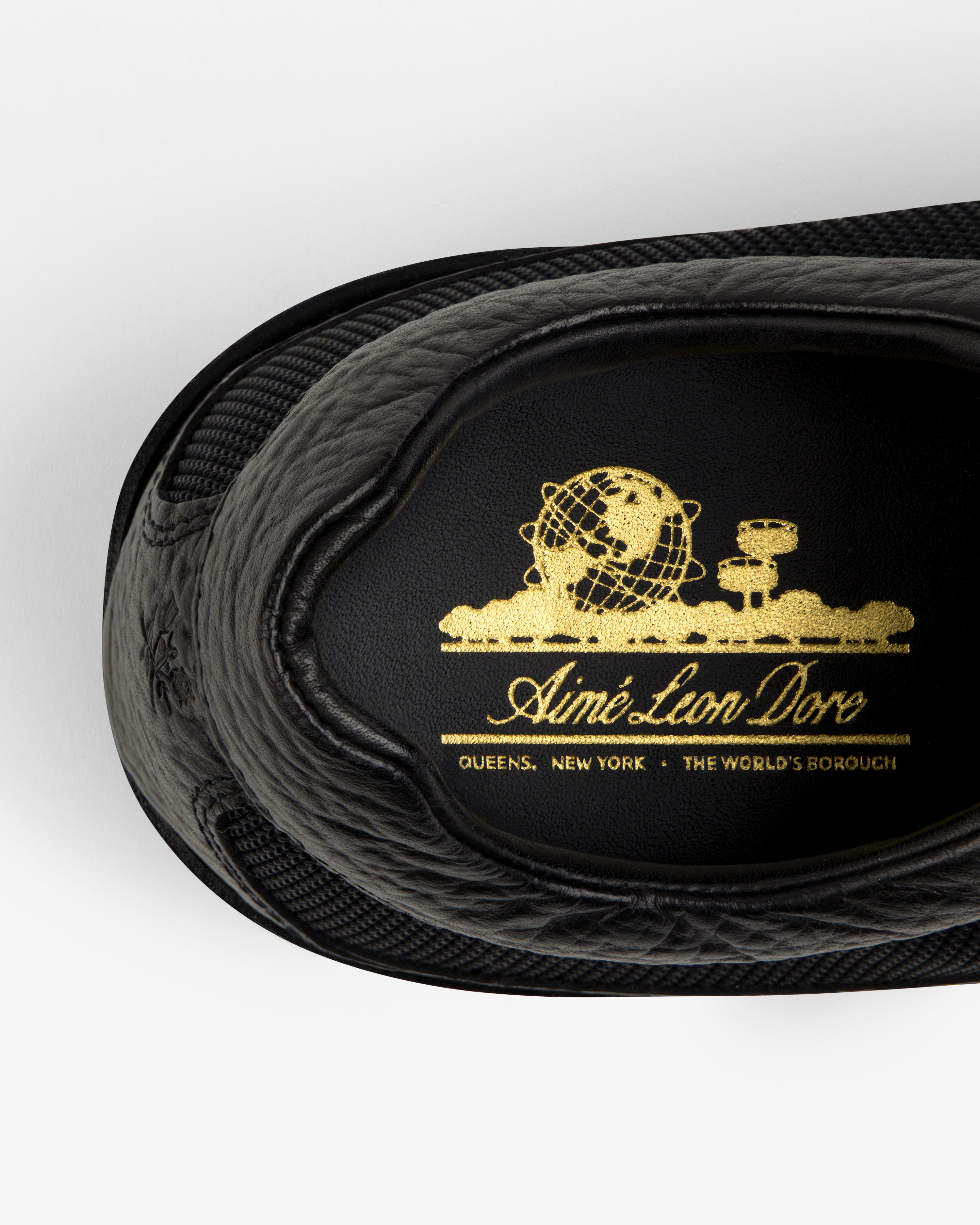 Black leather Field Boot insole with a gold globe emblem reading Aimé Leon Dore, Queens, New York.