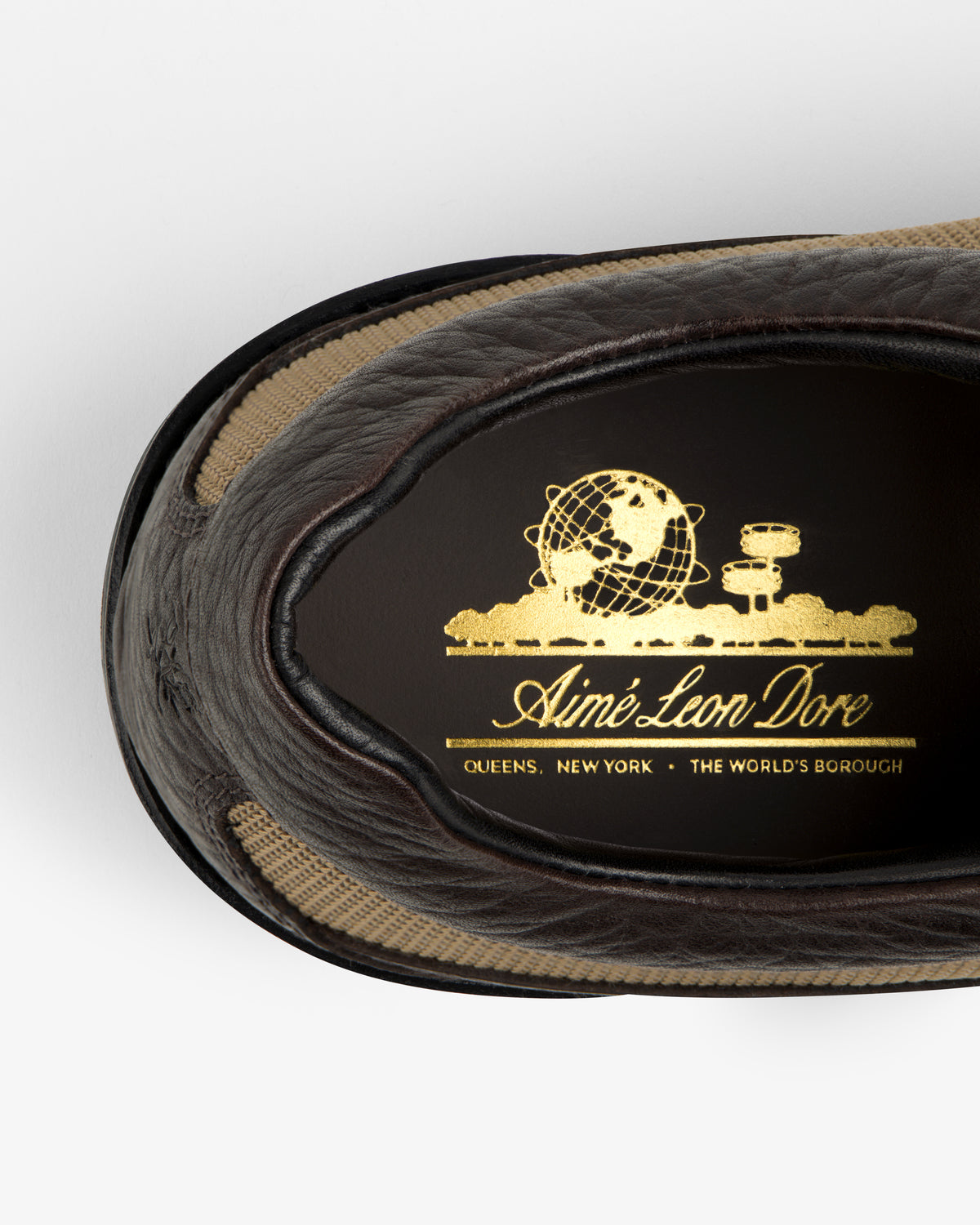 Interior view of a dark brown Field Boot featuring a gold globe emblem and the brand name Aimé Leon Dore.