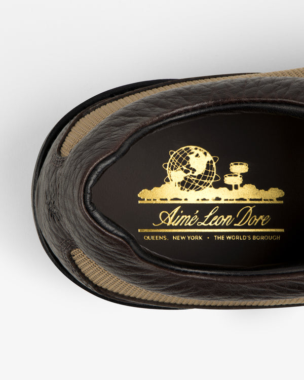 Interior view of a dark brown Field Boot featuring a gold globe emblem and the brand name Aimé Leon Dore.