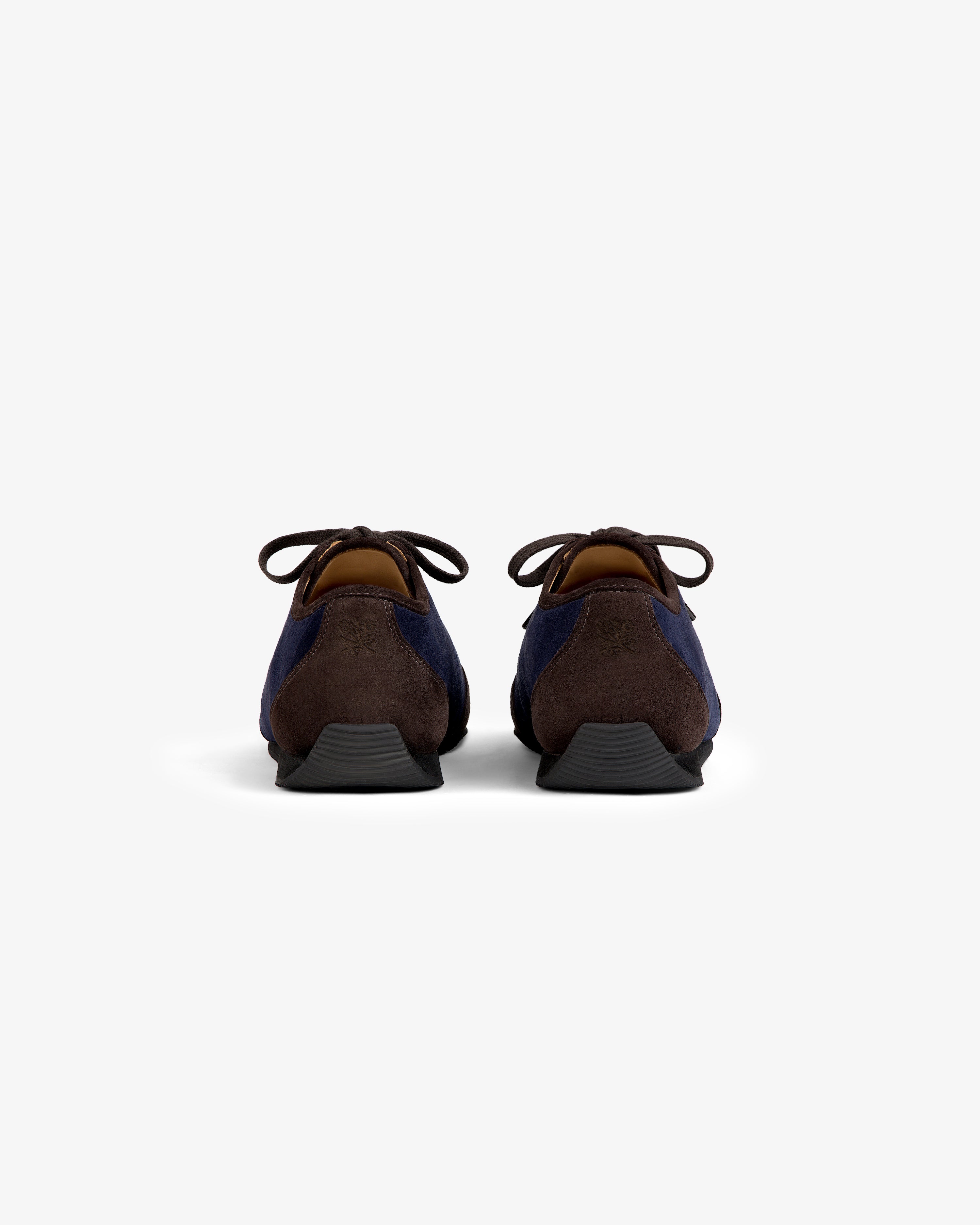 Back view of two Low Profile Suede Trainer navy and brown suede shoes with black soles.