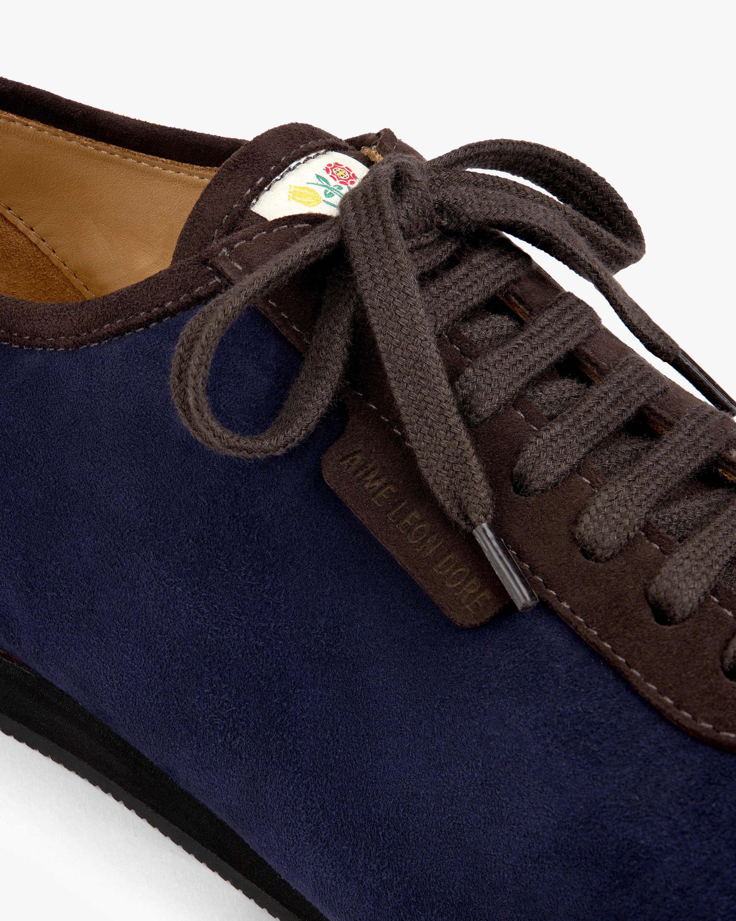 Low Profile Suede Trainer in navy blue suede with brown trim and laces, featuring a floral patch on the tongue.