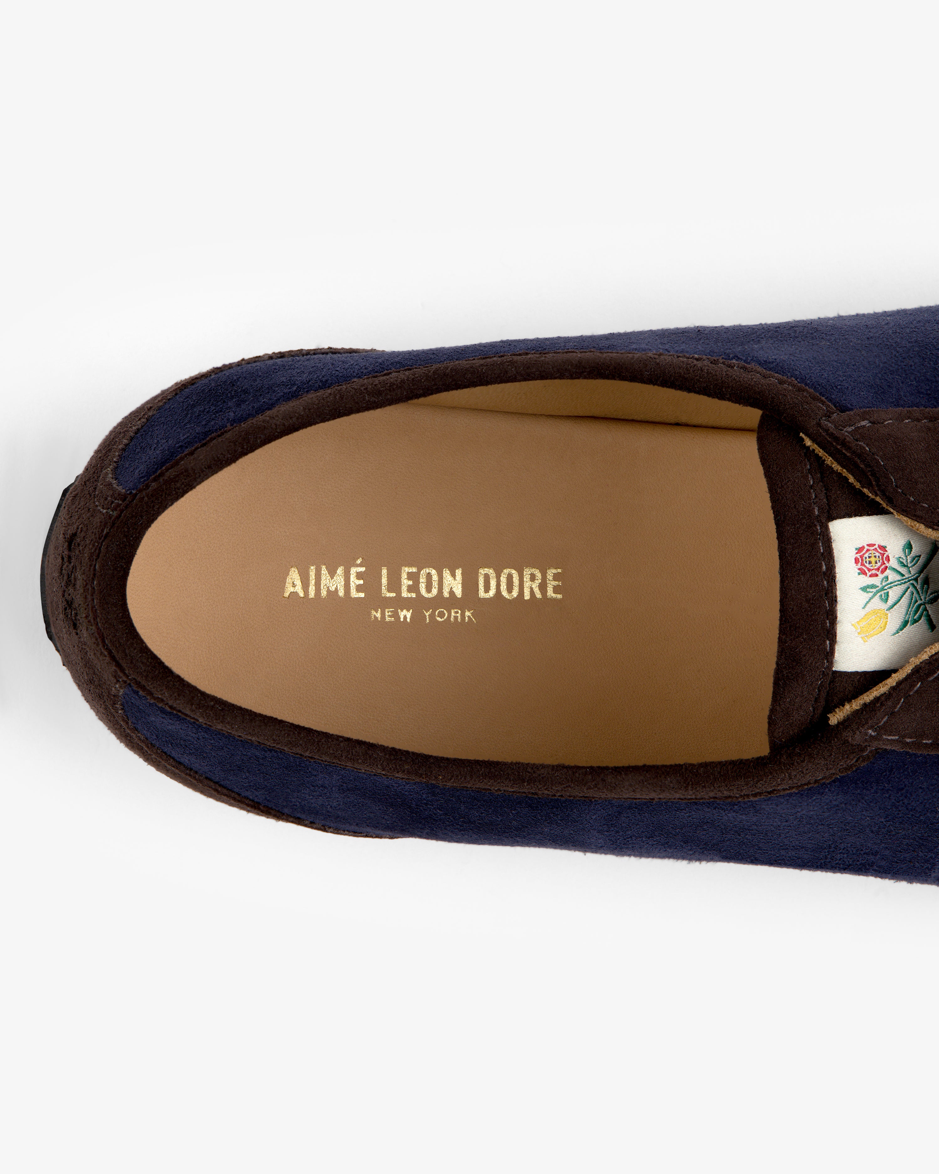 Top-down view of a navy Low Profile Suede Trainer showing the brand name on the insole and a flower patch on the tongue.