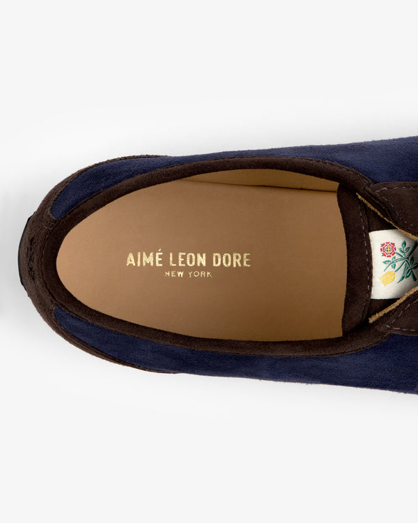 Top-down view of a navy Low Profile Suede Trainer showing the brand name on the insole and a flower patch on the tongue.