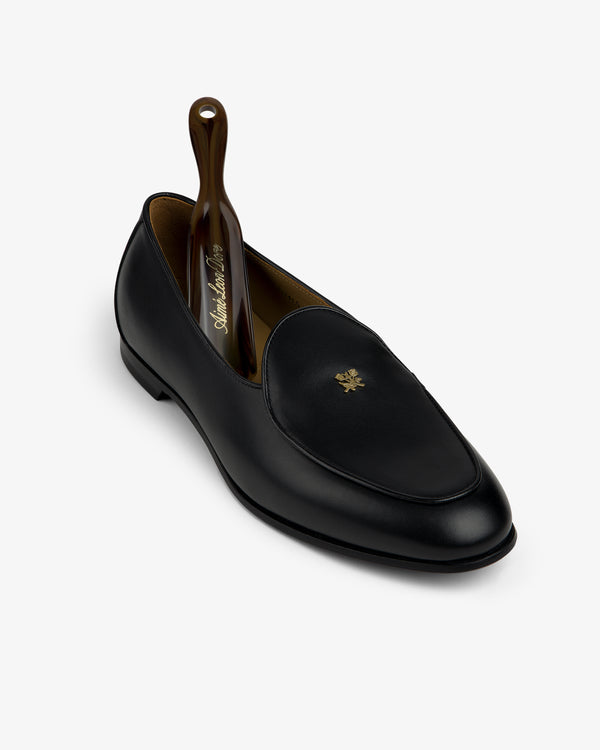 Crest Salóni Loafer: black leather with gold emblem and brown shoehorn, displayed on a white background.