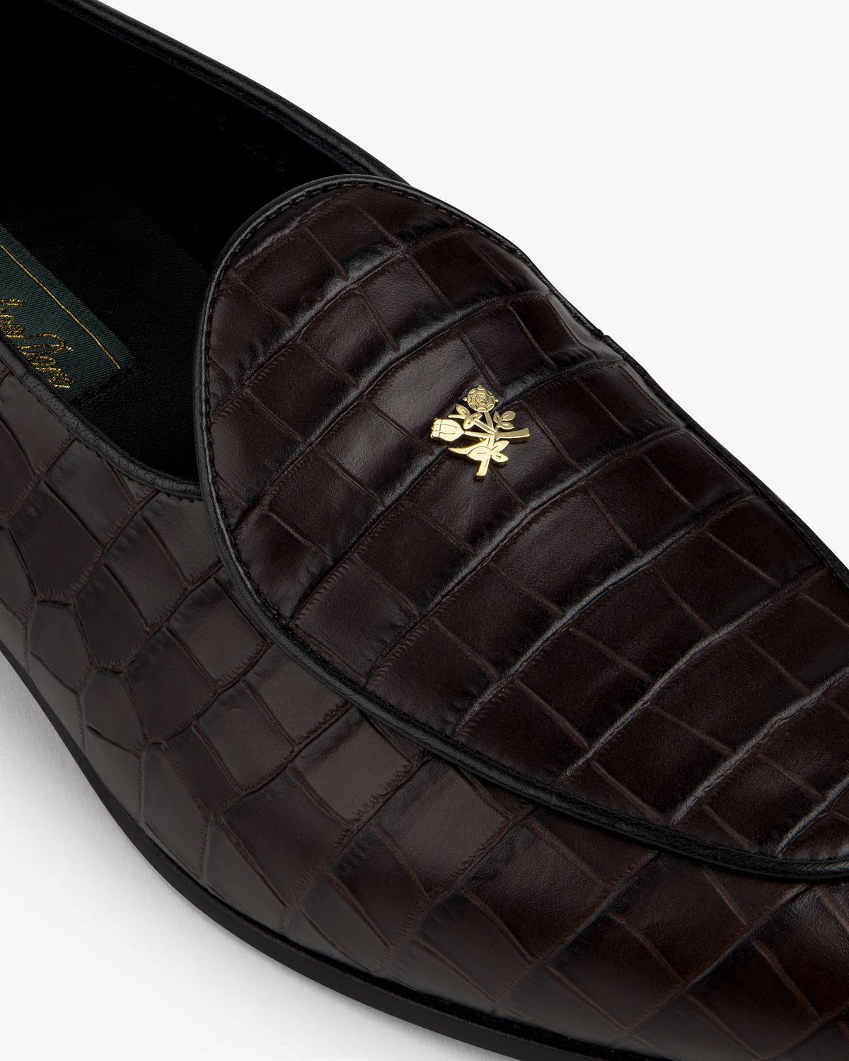 Close-up of the Croc-Embossed Crest Salóni Loafer featuring dark brown crocodile pattern and gold emblem.