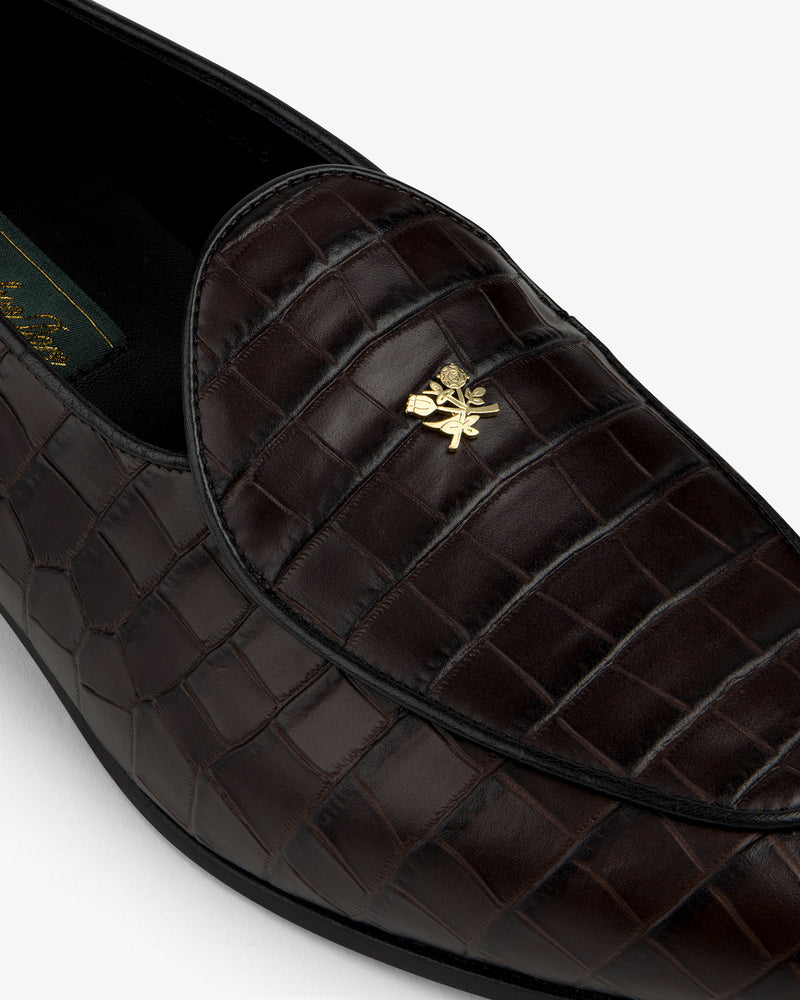 Close-up of the Croc-Embossed Crest Salóni Loafer featuring dark brown crocodile pattern and gold emblem.