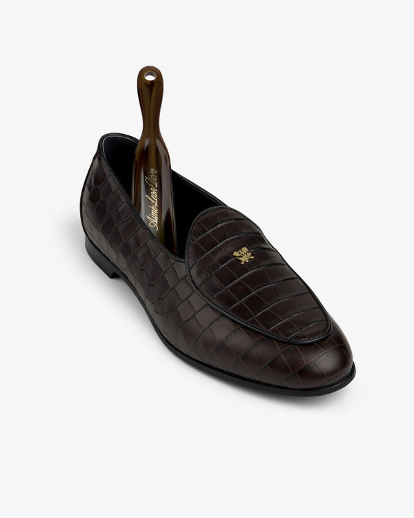Croc-Embossed Crest Salóni Loafer in brown with gold emblem, shown with shoehorn on a white background.