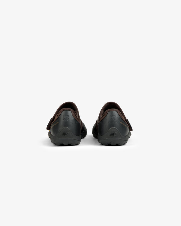 Rear view of two black ALD / New Balance MT2 slip-on shoes with dark brown trim and lugged outsoles.