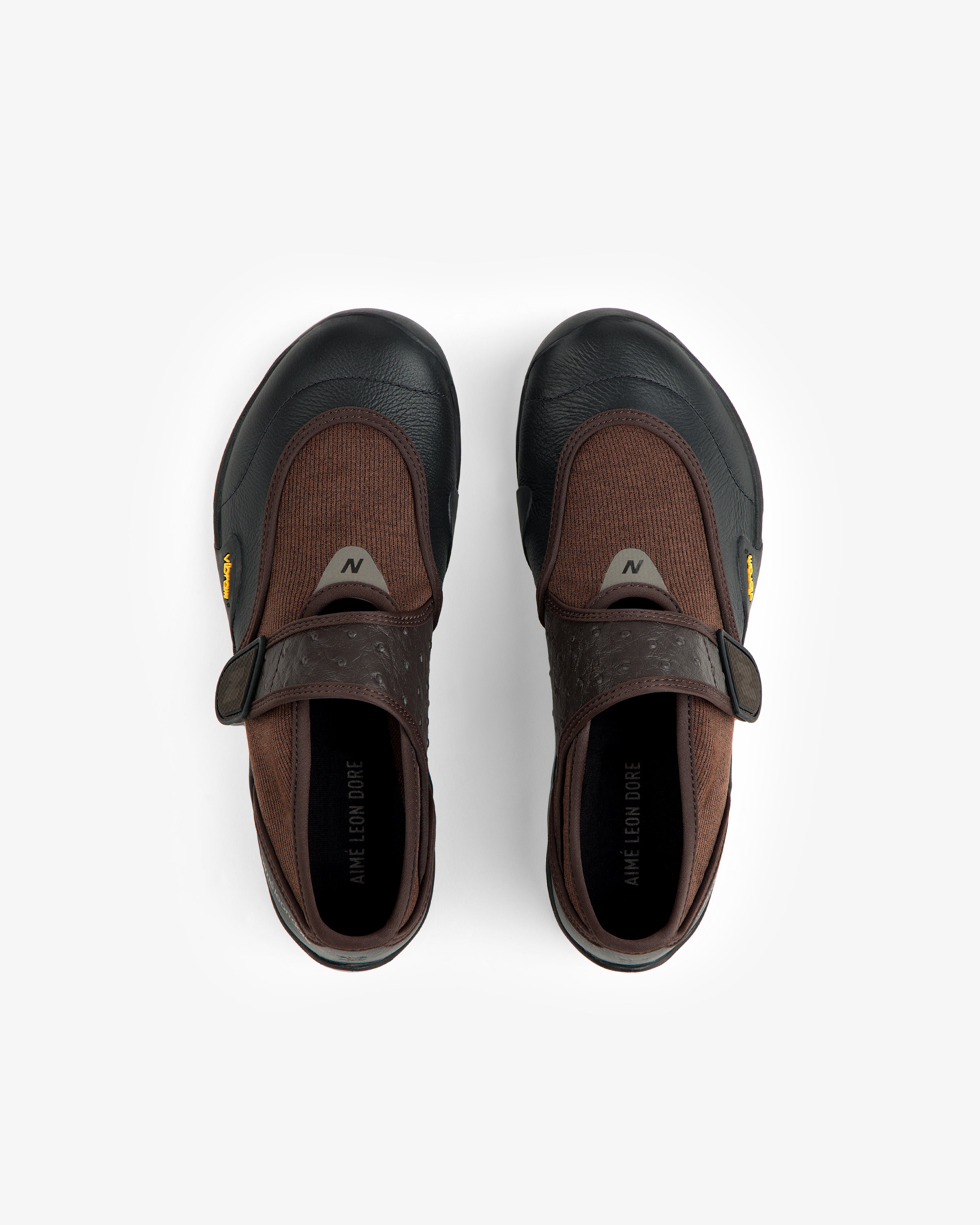 Top-down view of brown and black ALD / New Balance MT2 slip-on shoes with hook-and-loop closures and yellow Vibram tags.